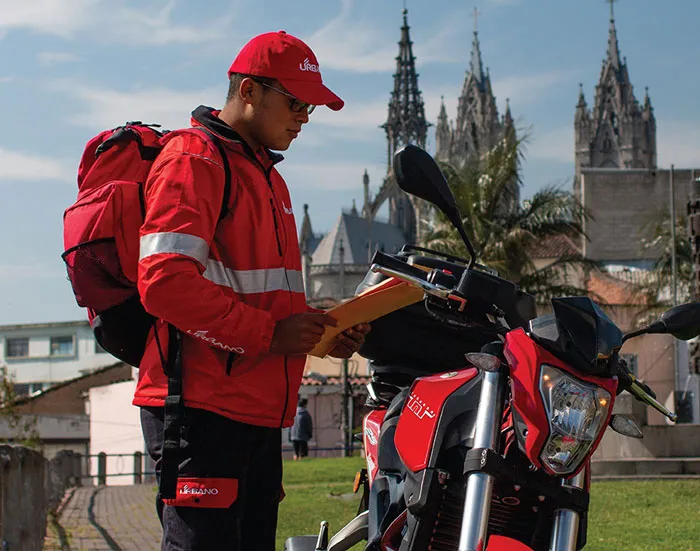 Seorang pengantar barang Urbano Envios berdiri di samping sepeda motor