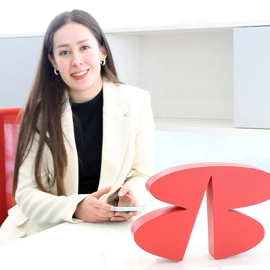 Una mujer vestida formalmente sosteniendo un teléfono móvil, sonriendo a la cámara