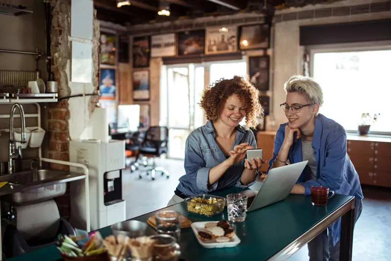 Duas pessoas em uma mesa de cozinha de escritório olhando para um celular
