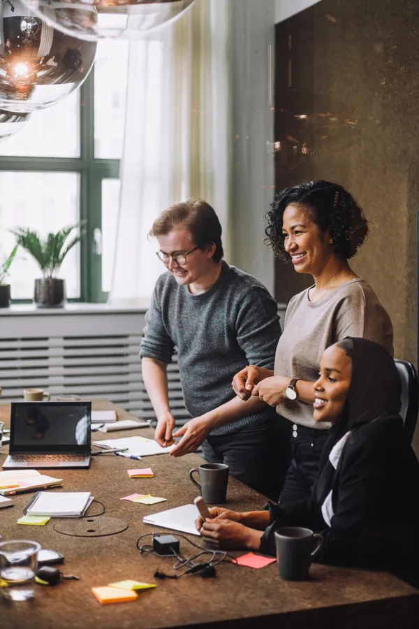 Seorang pria dan dua wanita berdiskusi di meja bersama orang yang tidak terlihat di sisi lain meja