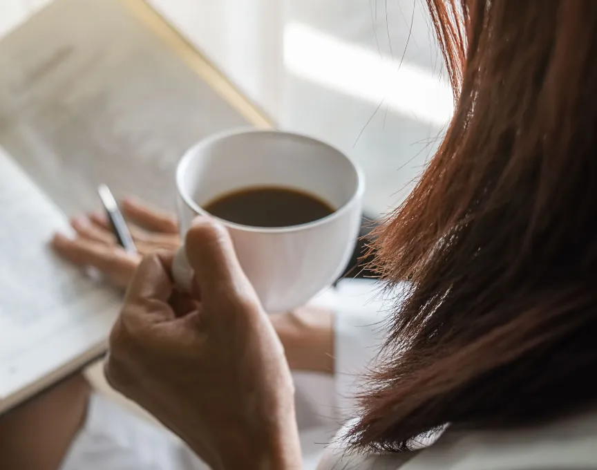 Seseorang sangat fokus membaca buku, sambil meminum secangkir kopi.