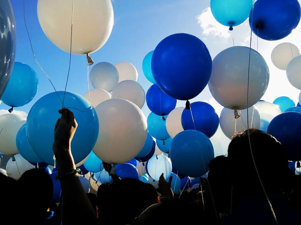 Foule de personnes tenant des ballons bleus et blancs dressés vers le ciel bleu