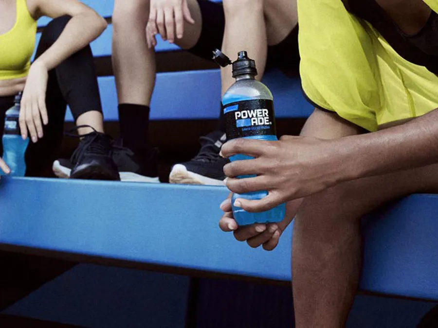 खेल के मैदान में स्टैंड्स पर बैठकर Powerade पीते हुए कुछ एथलीट